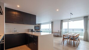 Une cuisine moderne avec des meubles de couleur sombre, un plan de travail blanc et un coin repas comprenant une table et des chaises en bois.