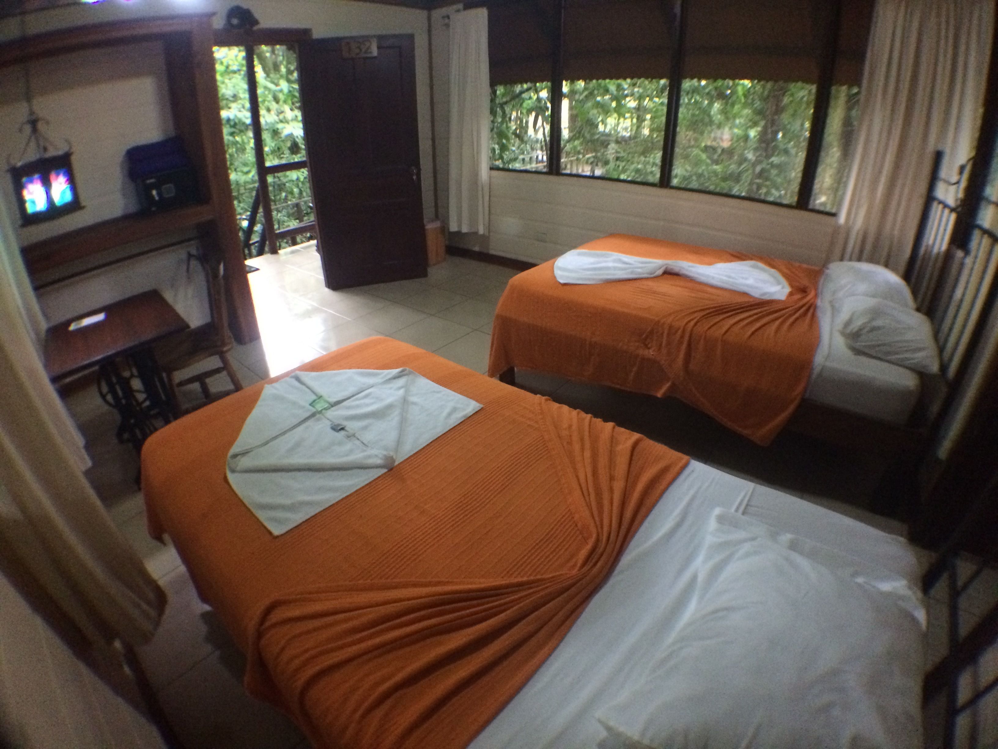 Una habitación con dos camas, un escritorio y una ventana con vista a árboles.