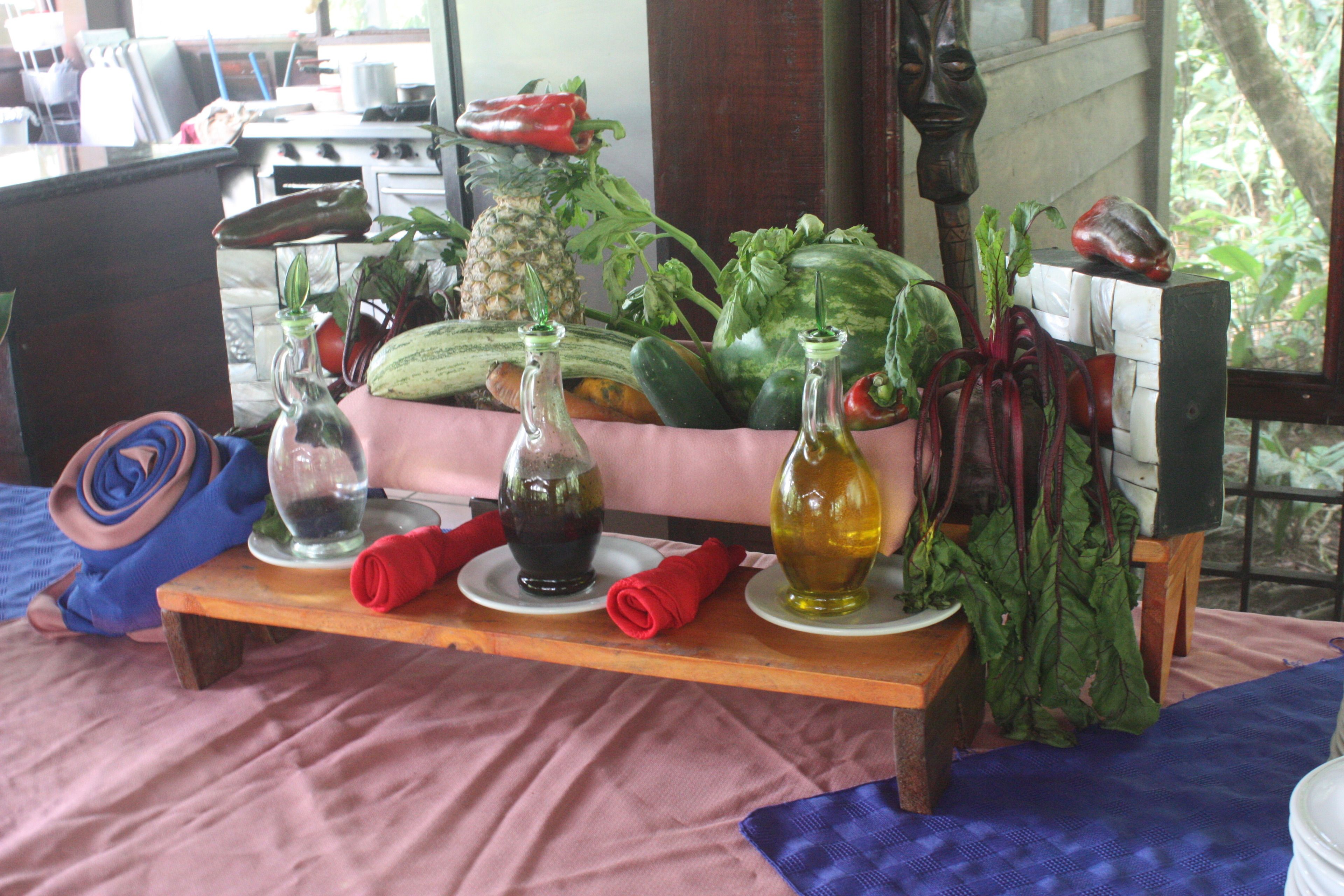 A kitchen counter with various vegetables, a pineapple, and two bottles of olive oil.