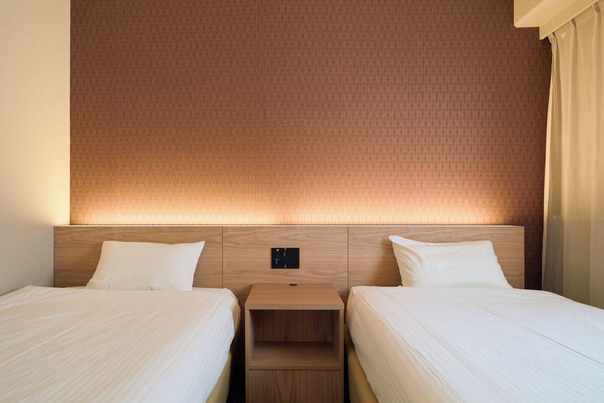 A hotel room with two beds, a headboard with a patterned design, and a nightstand between the beds.