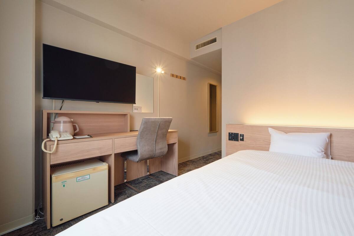 A hotel room with a bed, a desk with a chair, a television, a coffee maker, and a small refrigerator.