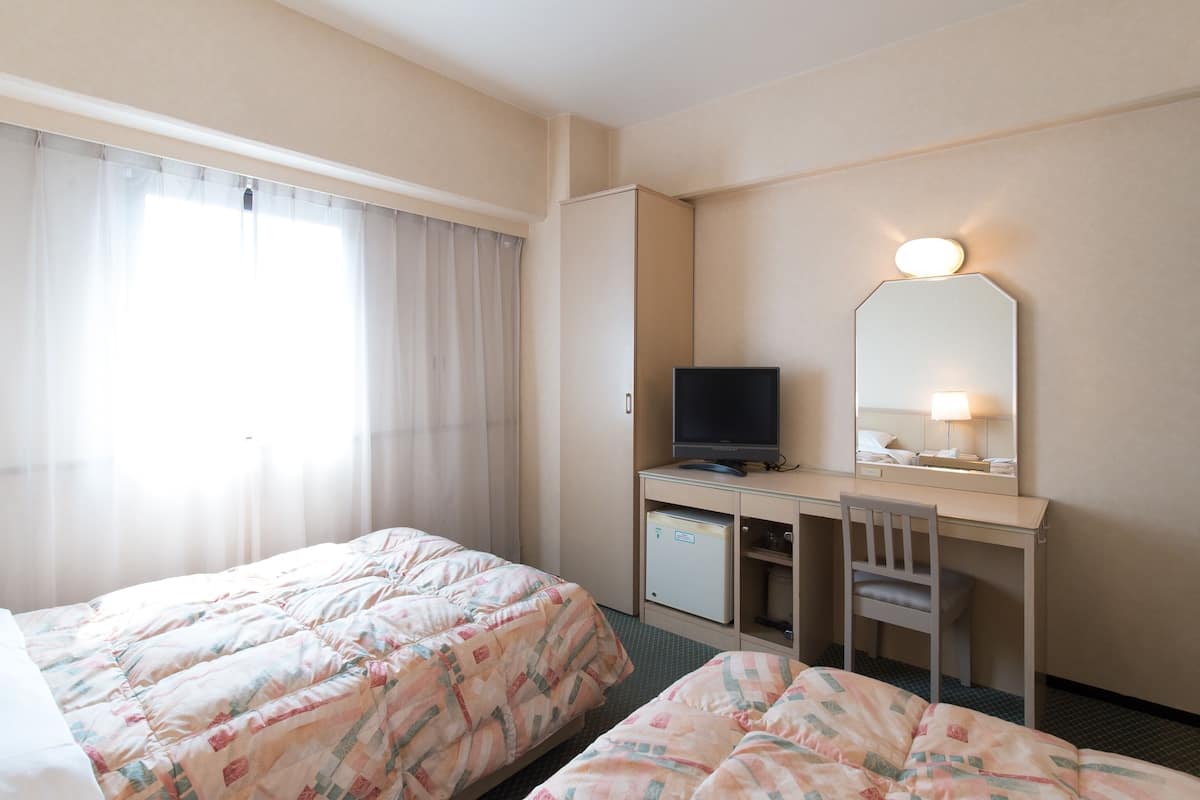 A hotel room with two beds, a desk with a TV, a mirror, and a small cabinet.