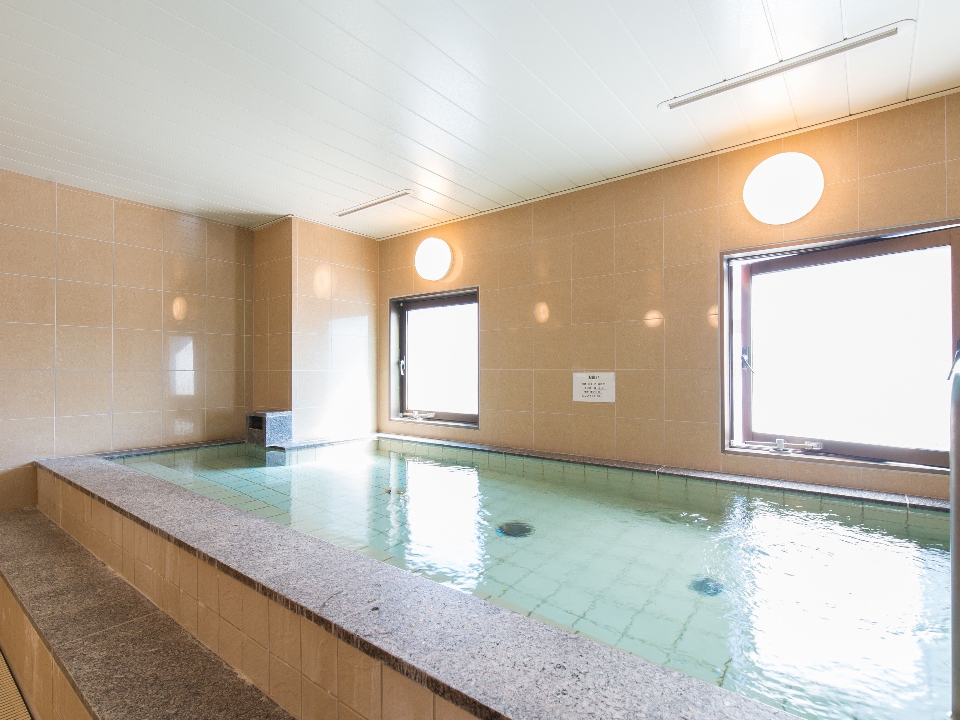 A swimming pool with tiled walls and a tiled floor, surrounded by a stone border.