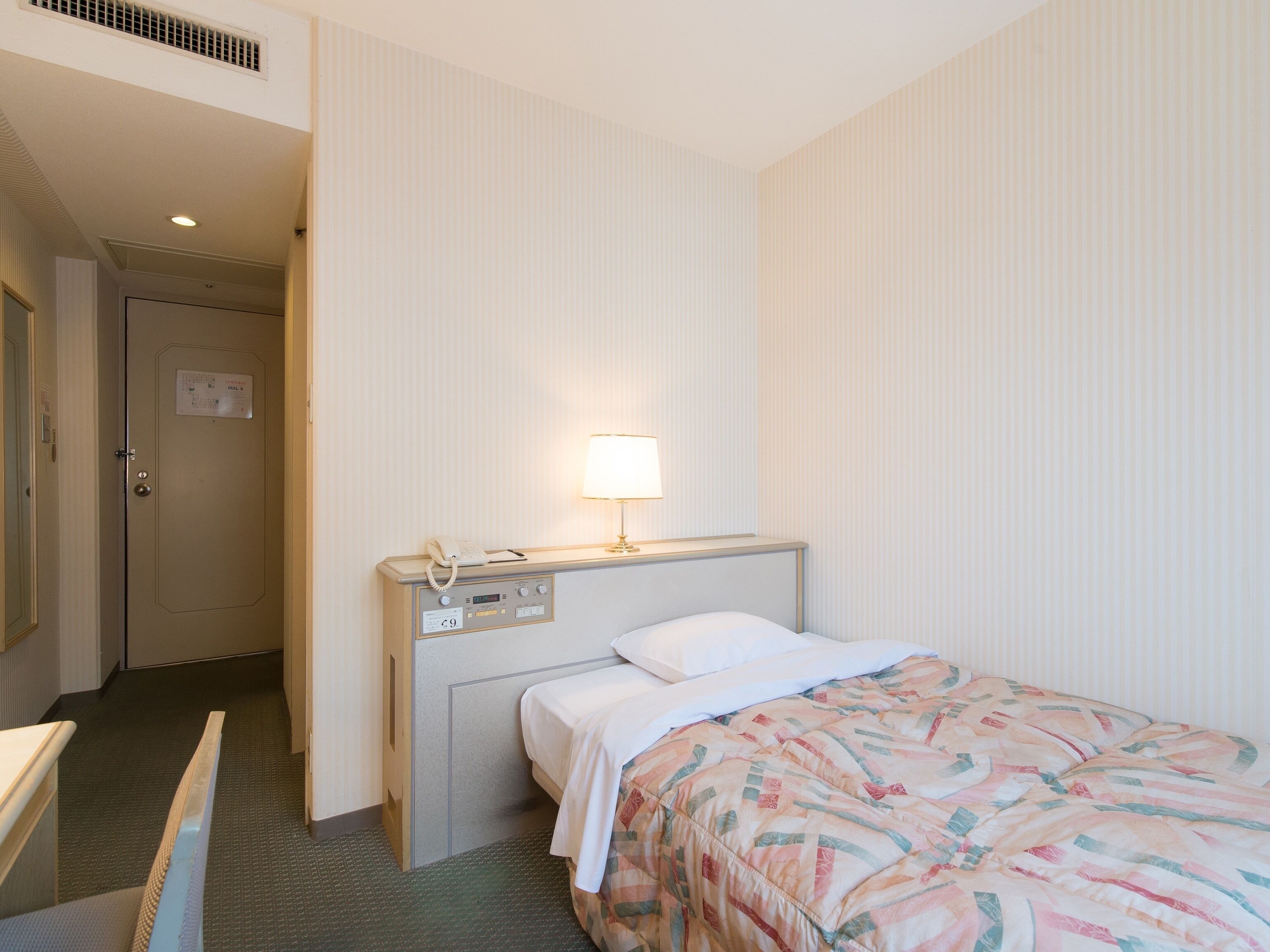 A hotel room with a bed, bedside table, lamp, and a telephone.