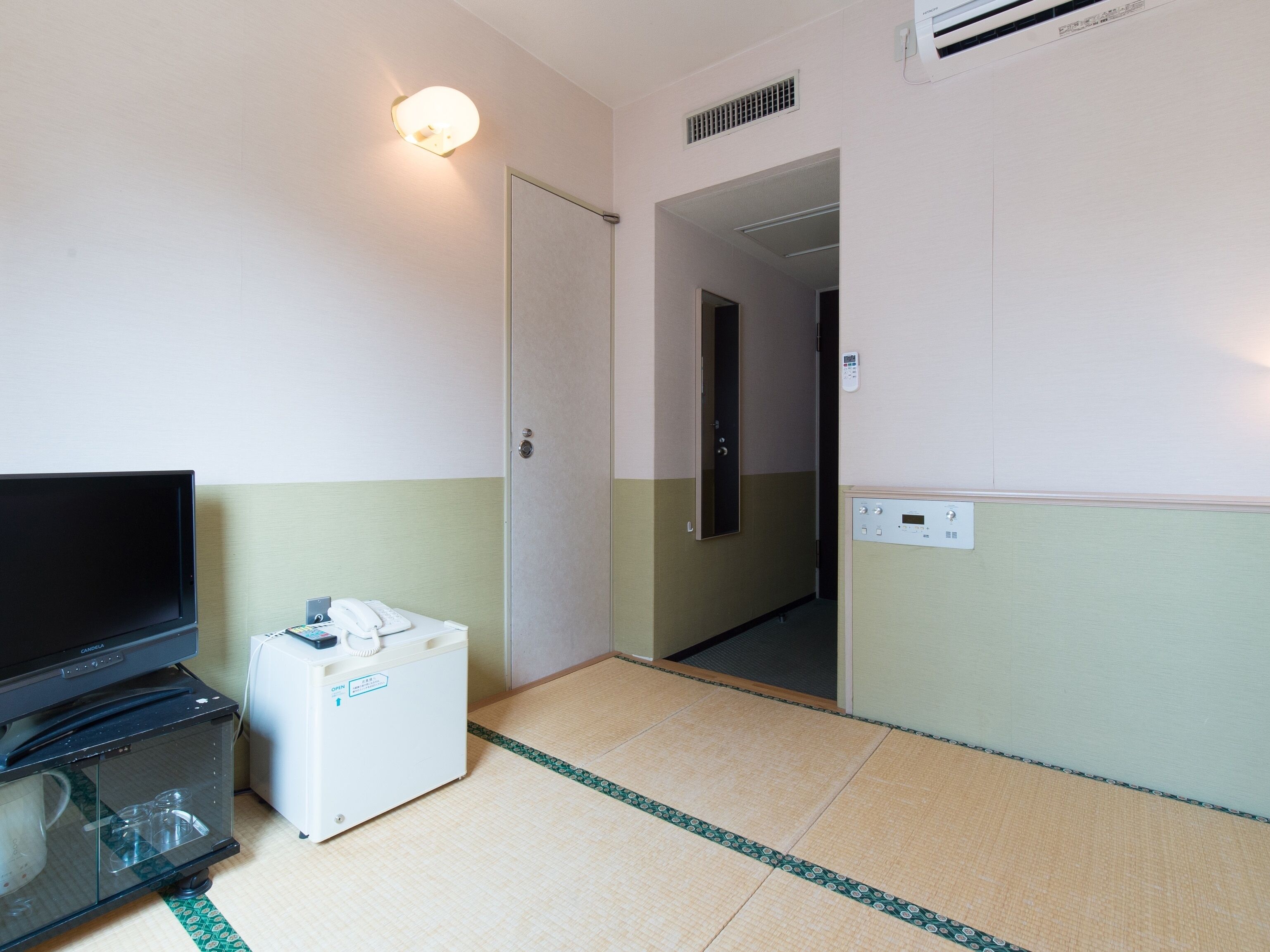 A hotel room with a television, a minibar, a door, and a wall-mounted air conditioning unit.