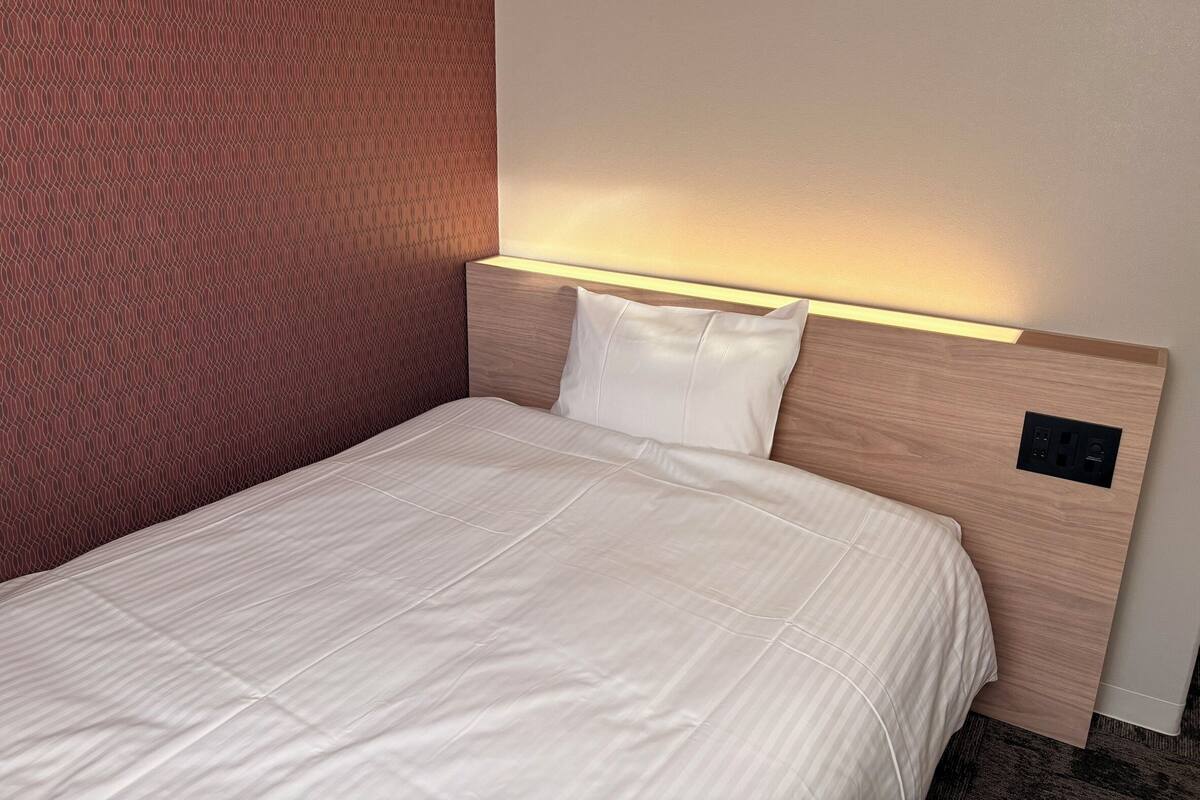 A hotel room with a neatly made bed, a headboard with integrated lighting, and a patterned wall.