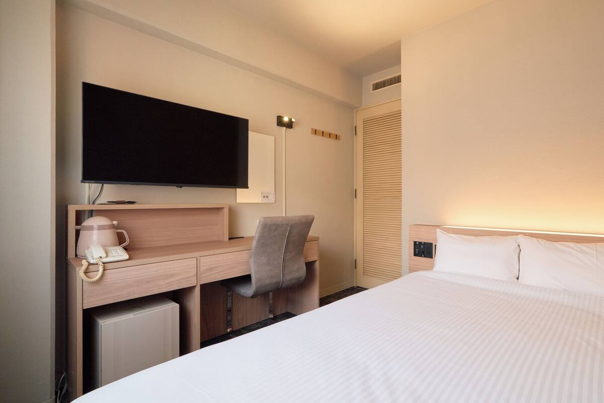 A hotel room with a bed, a desk with a chair, a television, and a wardrobe.