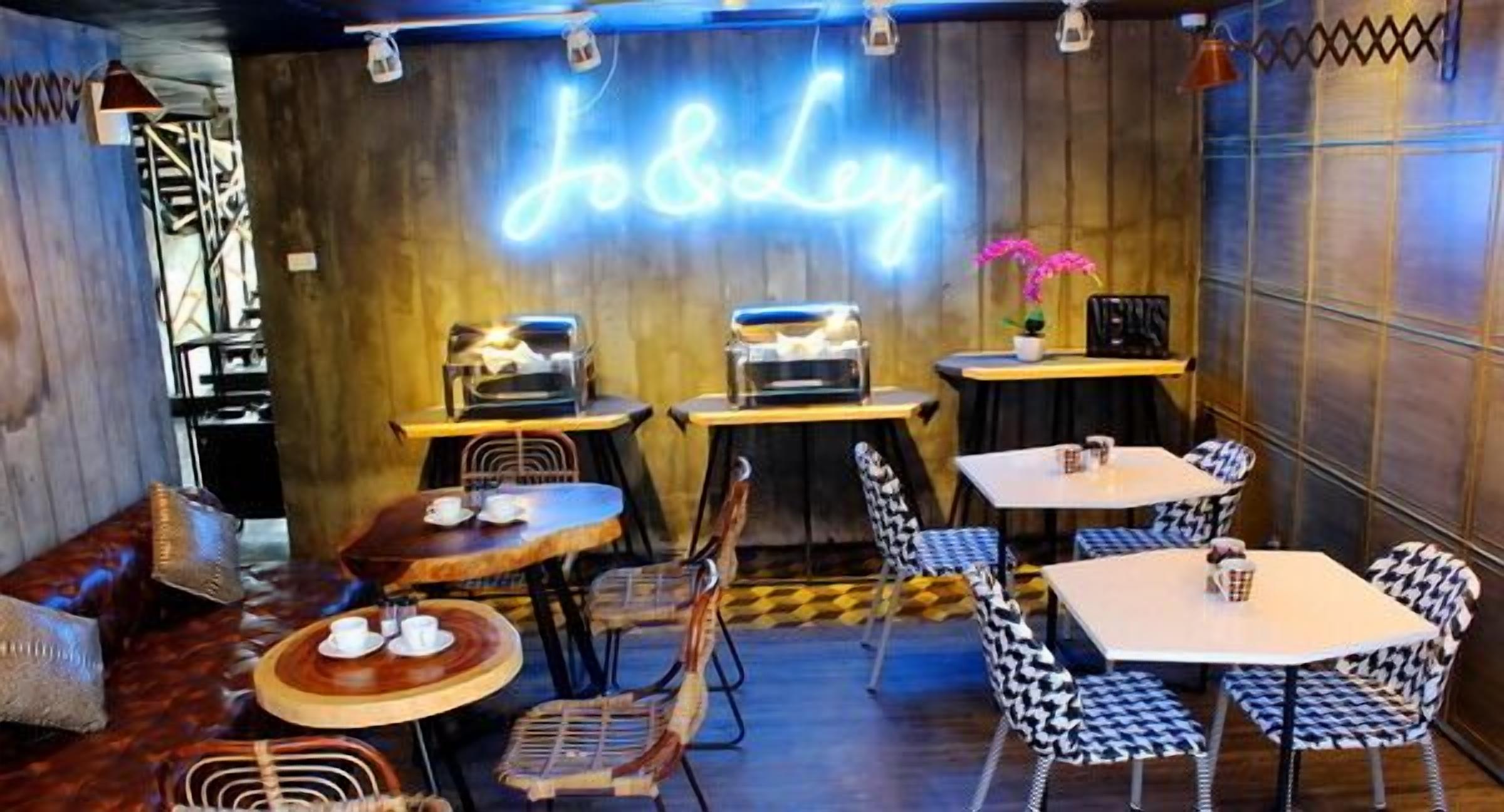 A cozy restaurant interior with wooden walls, neon 'J&L' sign, and a mix of wooden and metal furniture.