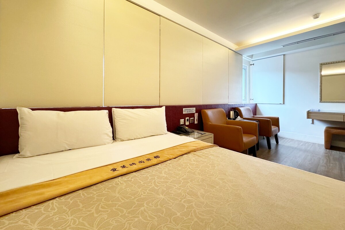 Een hotelkamer met een bed, twee stoelen, een tafeltje en een spiegel.