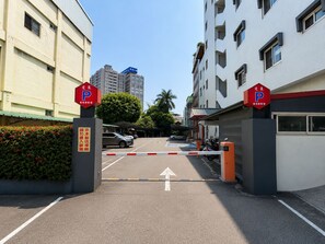 Een omheind parkeerterrein met een duidelijke weg die leidt naar een parkeerplaats, omringd door gebouwen en groen.