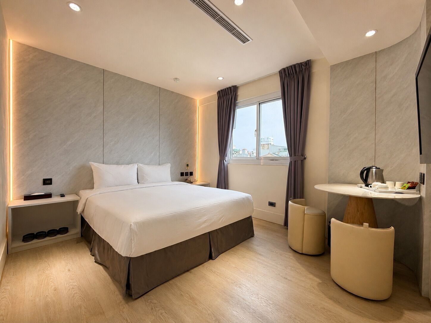 Une chambre moderne avec un grand lit, des tables de chevet, une coiffeuse avec un miroir et une fenêtre avec des rideaux.
