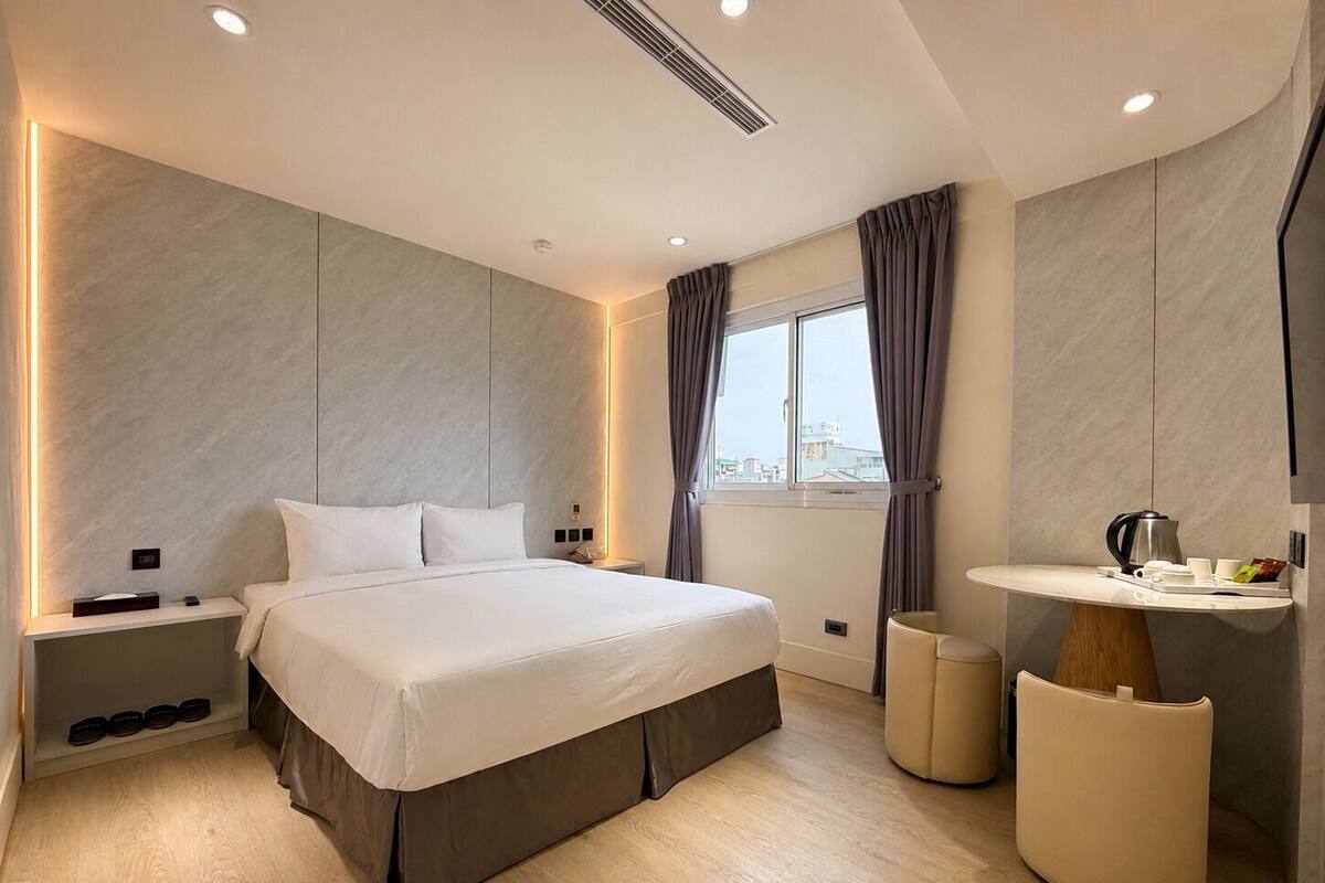 Une chambre moderne avec un grand lit, des tables de chevet, une coiffeuse avec un miroir et une fenêtre avec des rideaux.