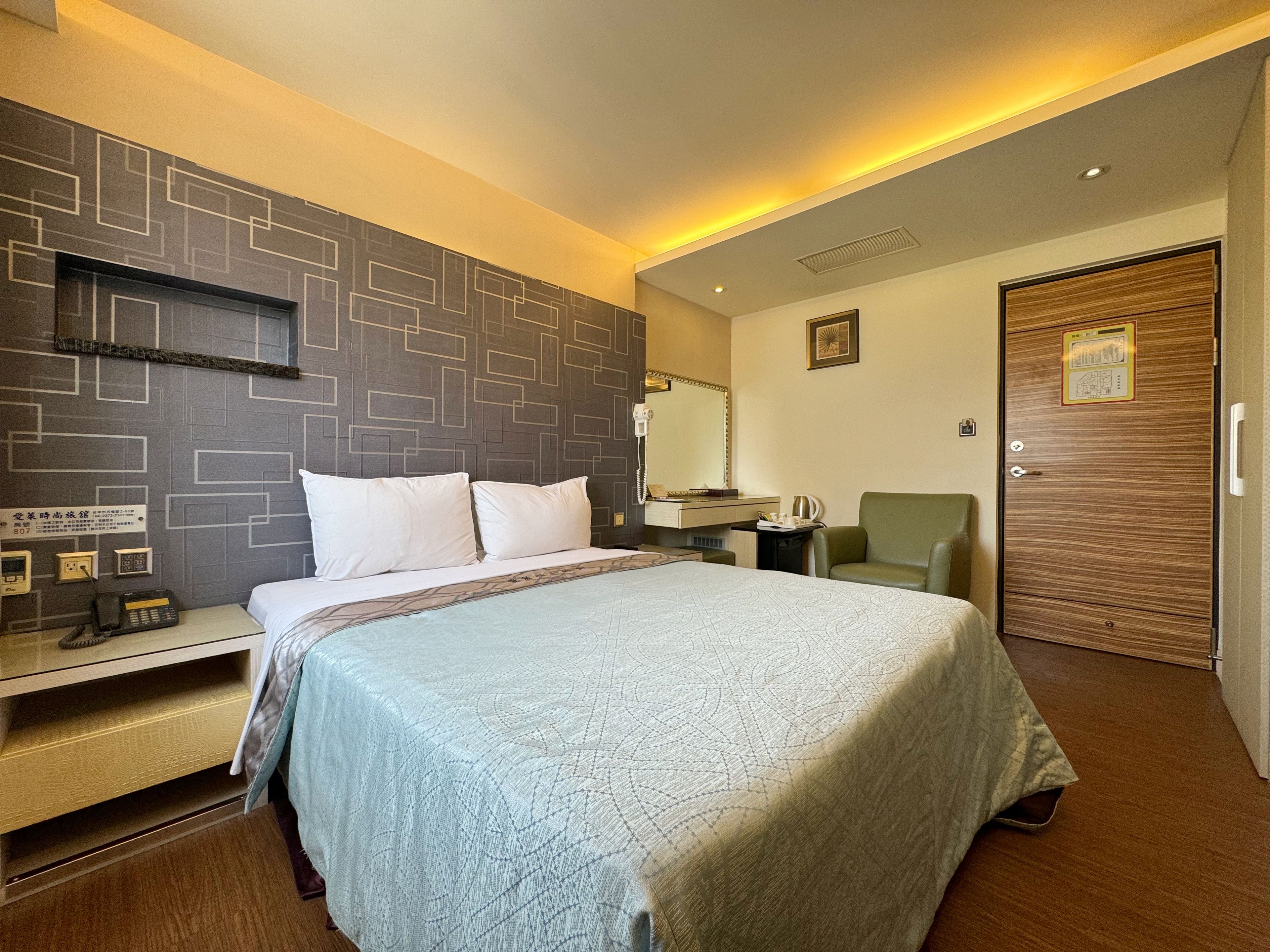 Une chambre d’hôtel avec un lit, une table de chevet, une chaise et une porte en bois.