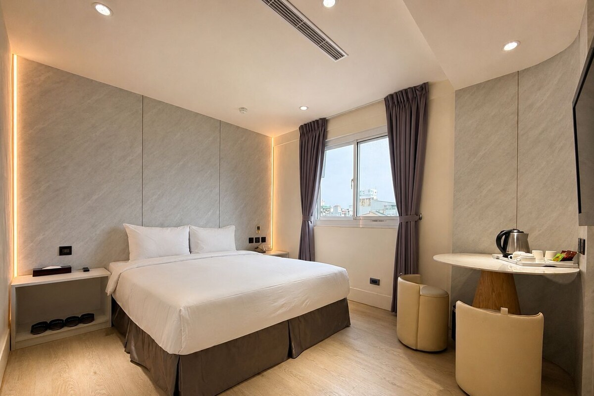 Een moderne slaapkamer met een groot bed, nachtkastjes, een kaptafel met spiegel en een raam met gordijnen.
