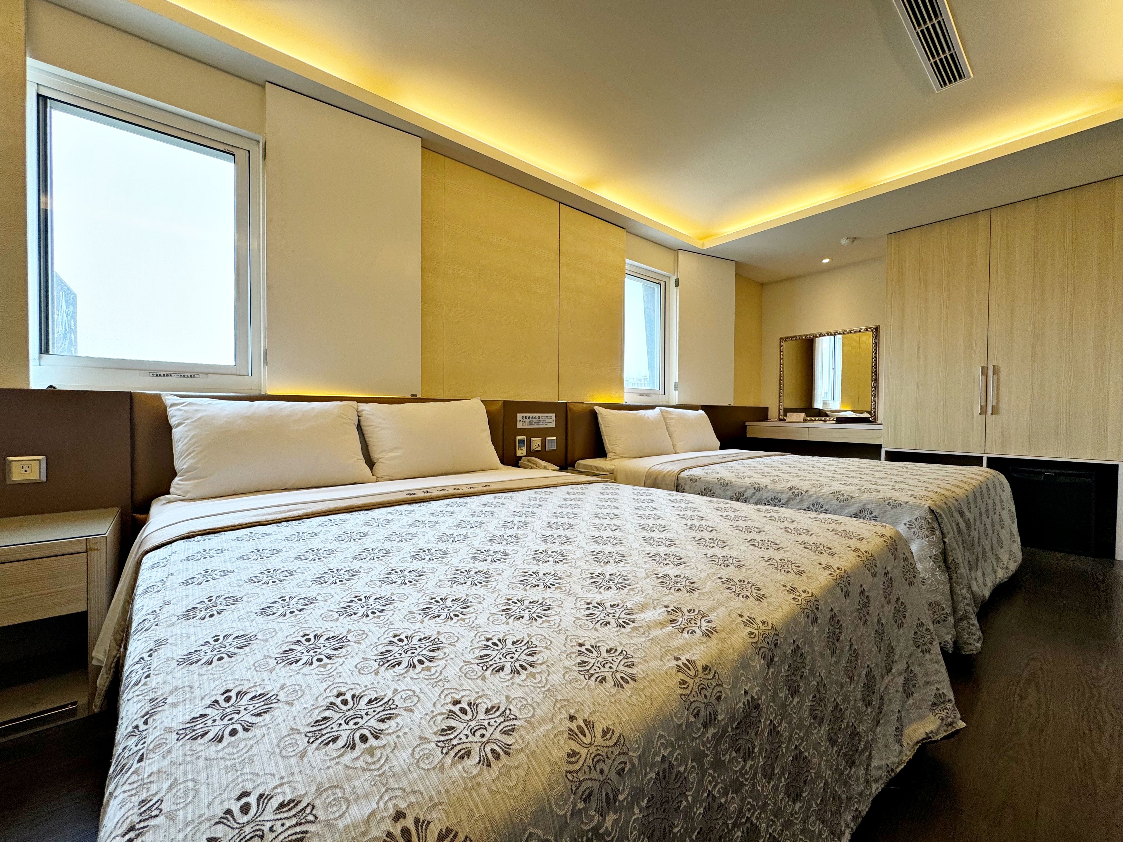A hotel room with two beds, bedside tables, a mirror, and a wardrobe.