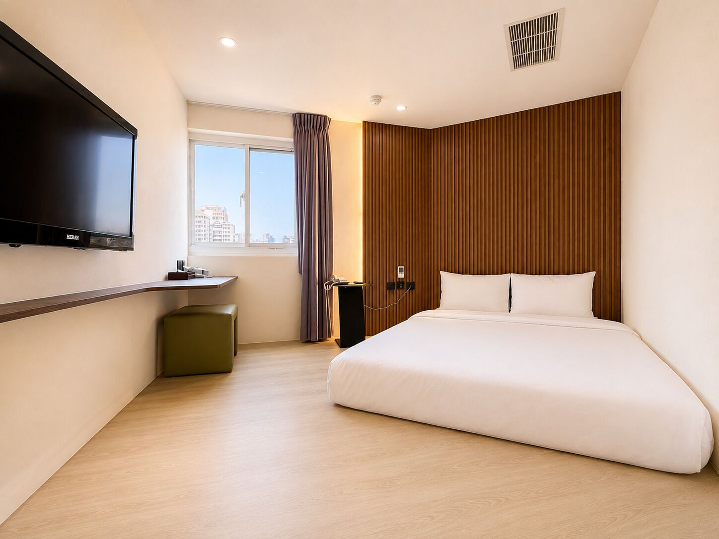 Une chambre d’hôtel avec un lit, un téléviseur fixé au mur, un bureau et une fenêtre avec des rideaux.