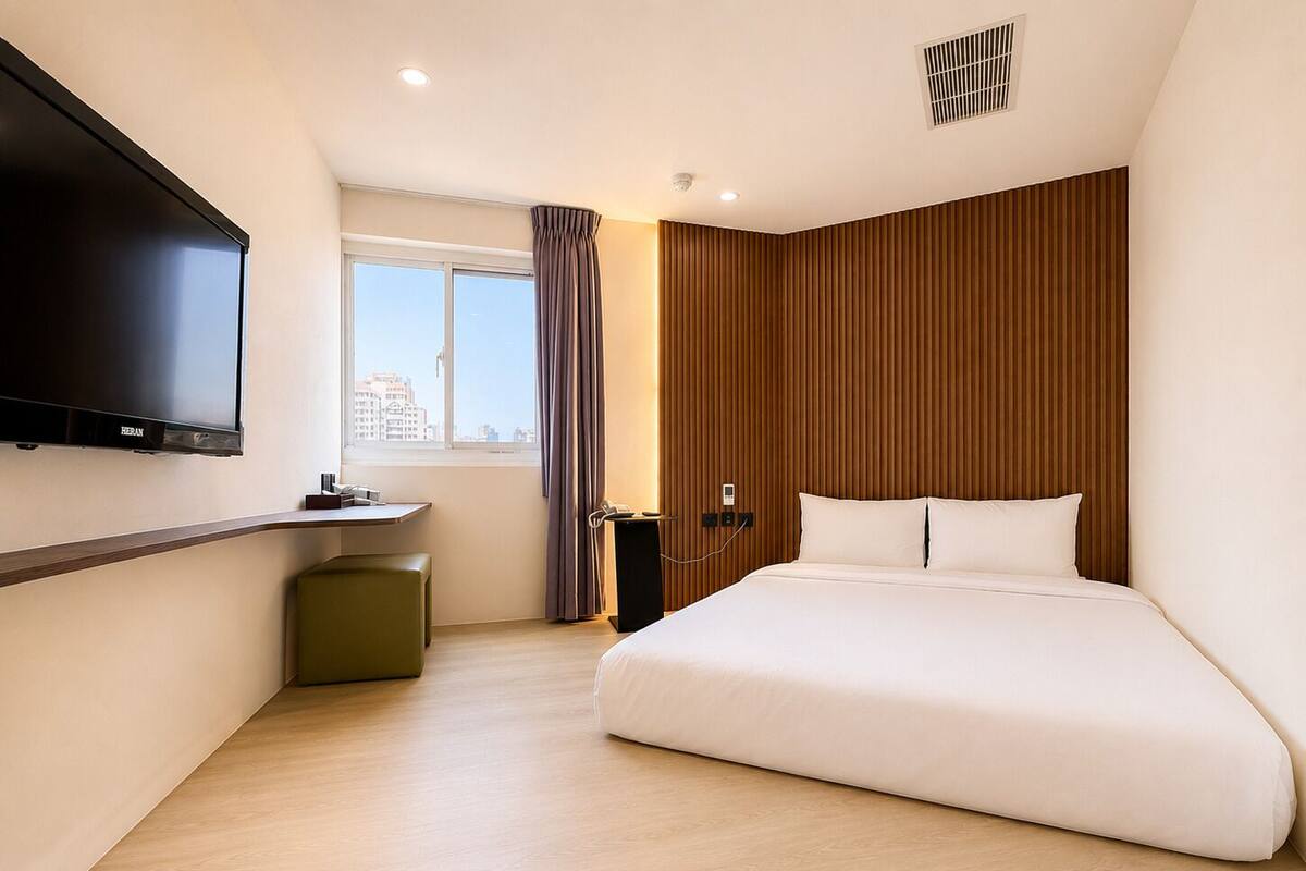 Une chambre d’hôtel avec un lit, un téléviseur fixé au mur, un bureau et une fenêtre avec des rideaux.
