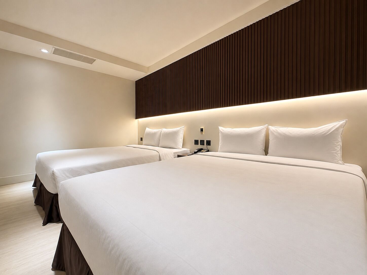 Une chambre d’hôtel avec deux lits, un mur recouvert de panneaux en bois et un design moderne.