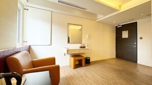 Une chambre d’hôtel avec un plancher en bois, un bureau avec une chaise, un miroir, une coiffeuse avec un lavabo et une porte.