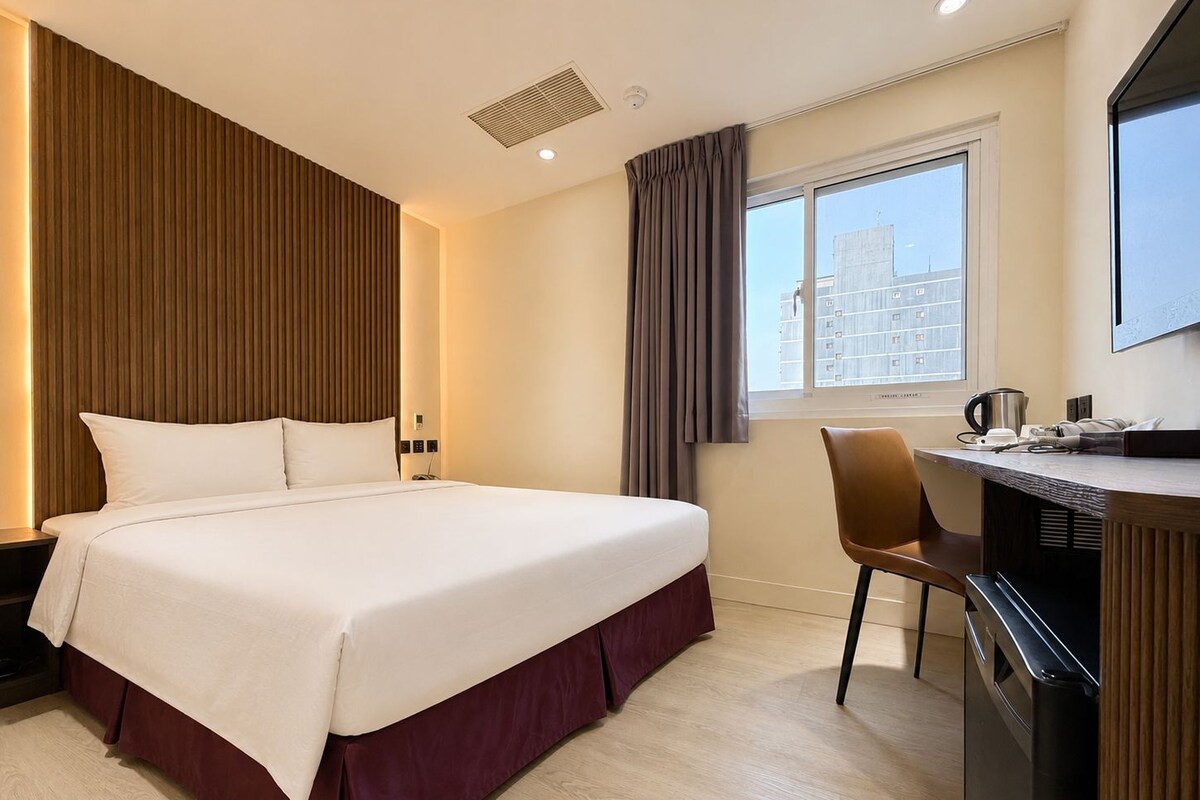 Een hotelkamer met een bed, een bureau, een stoel, een koffiezetapparaat en een raam met gordijnen.