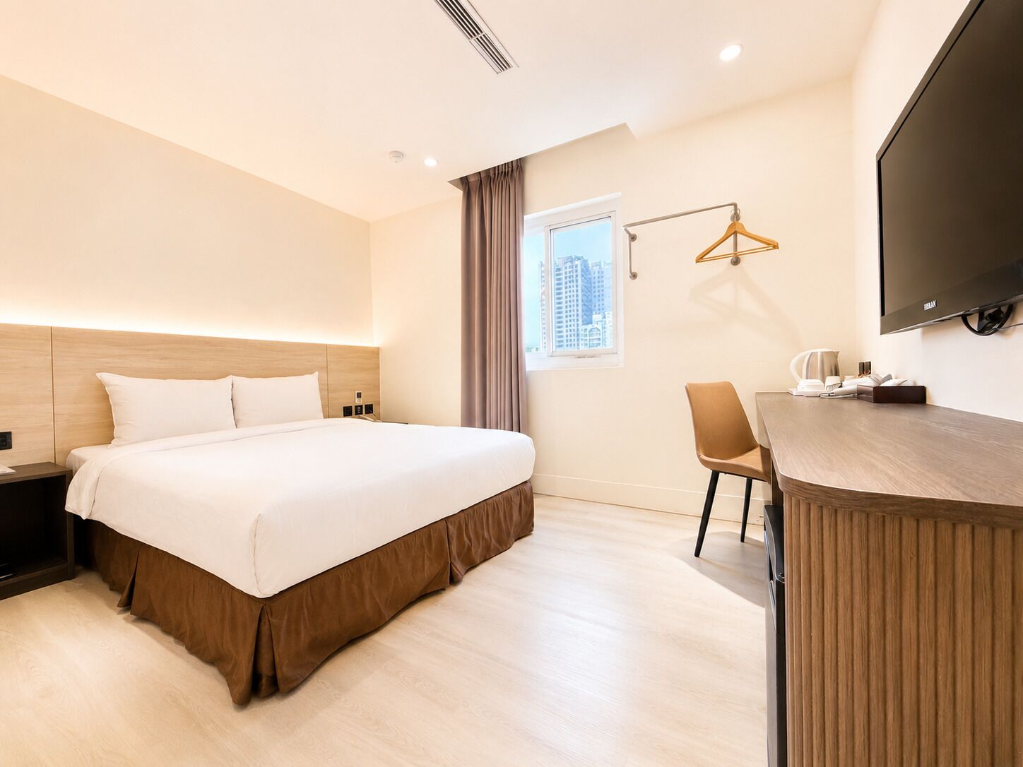 Une chambre d’hôtel comprenant un lit, une table de chevet, une chaise, un bureau, une télévision et une fenêtre avec des rideaux.