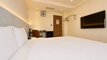 A hotel room with a large bed, a desk with a chair, a television, and a door with a coat rack.