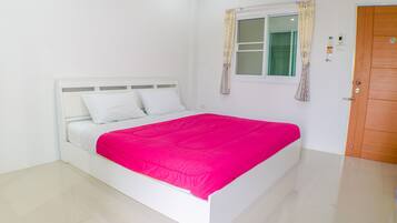 A white bed with a bright pink bedspread in a room with white walls and a wooden door.