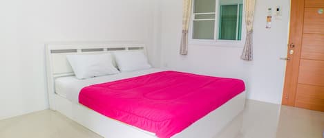A white bed with a bright pink bedspread in a room with white walls and a wooden door.