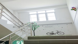A staircase with metal railings and a wall mural featuring a tree, birds, and a bicycle. - Be My Guest (Ubon Ratchathani)