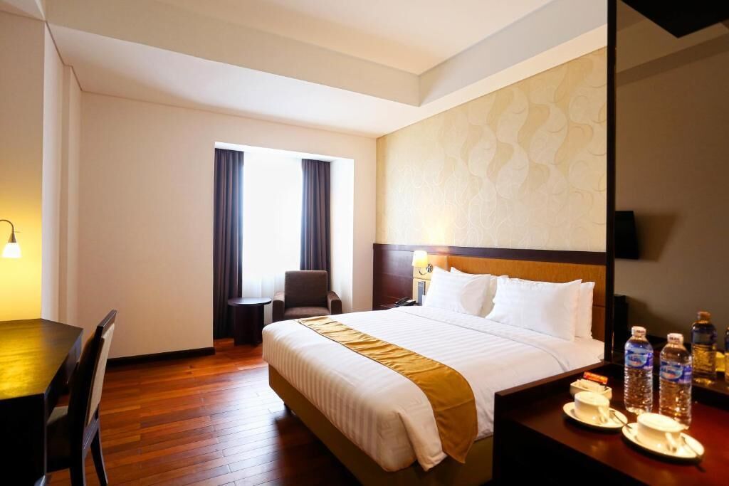 A hotel room with a large bed, a desk, a chair, a small table, and a window with curtains.