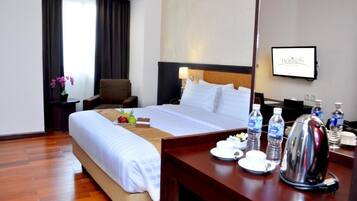 A hotel room with a bed, a desk with a kettle, water bottles, and a TV on the wall.