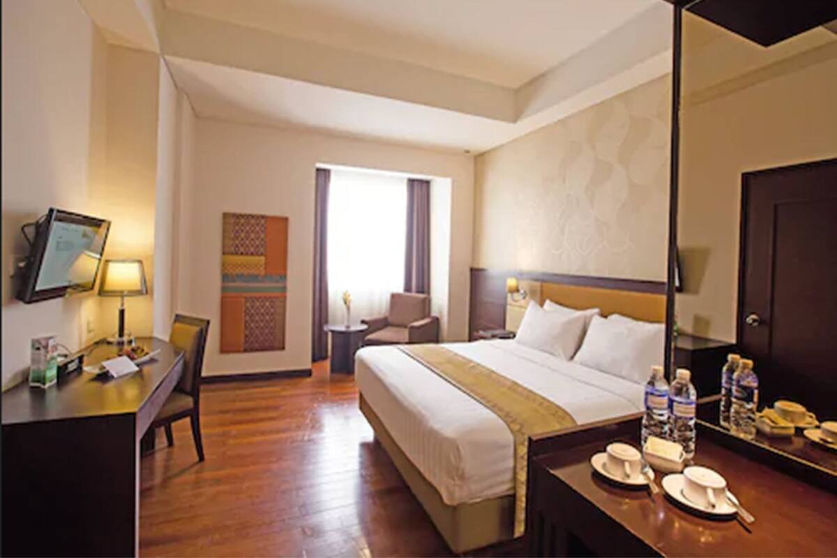 A hotel room with a bed, bedside table, desk, chair, and a large mirror.