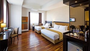 A hotel room with two beds, a desk, a chair, a TV, and a minibar. - Beston Hotel Palembang (Palembang)