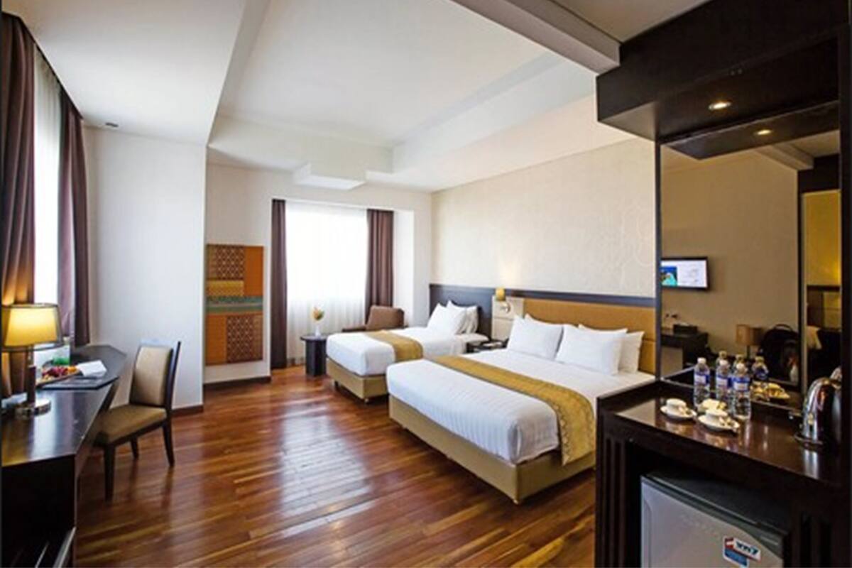 A hotel room with two beds, a desk, a chair, a TV, and a minibar.