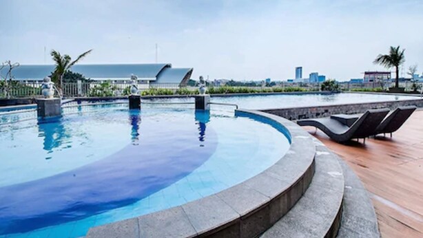 A swimming pool with a curved edge, lounge chairs, and a view of the ocean and city skyline. - Beston Hotel Palembang (Palembang)