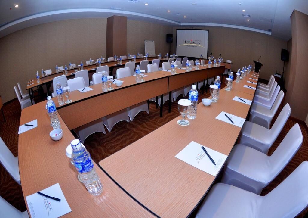 A conference room with a long table, chairs, water bottles, and a projector screen.