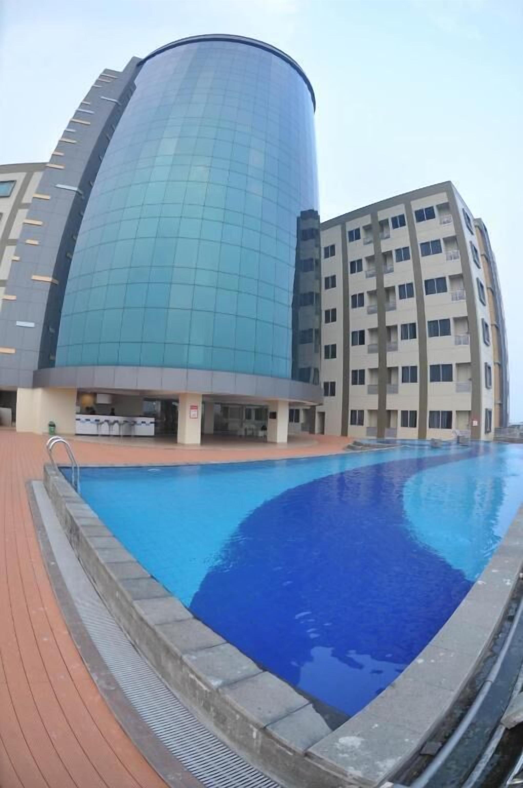 A modern building with a curved glass facade and a swimming pool in front.