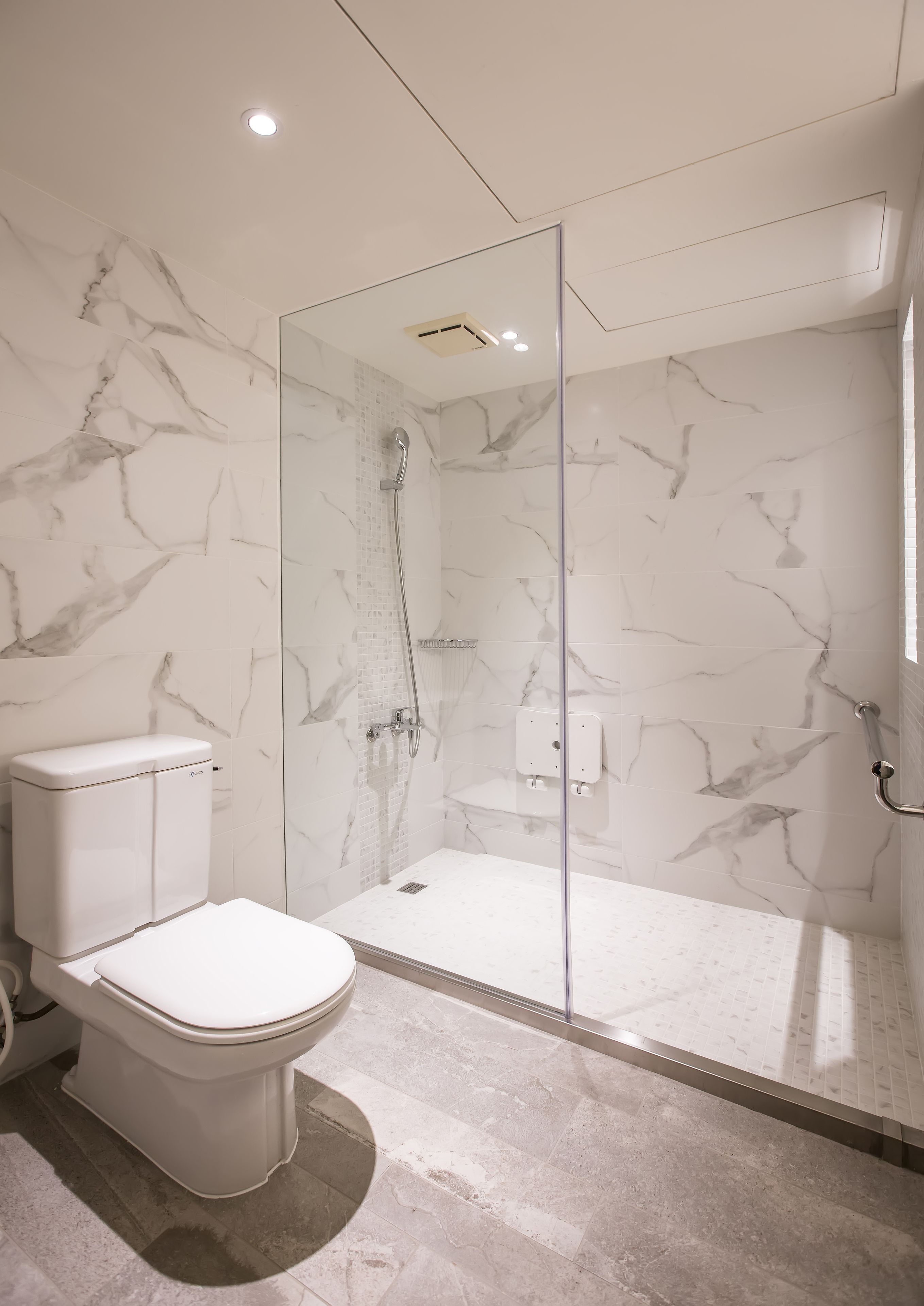 Et moderne badeværelse med bruseniche i glas, marmorvægge og et hvidt toilet.