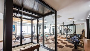 Ett gym med olika typer av träningsutrustning, stora fönster och ett rutmönstrat golv.