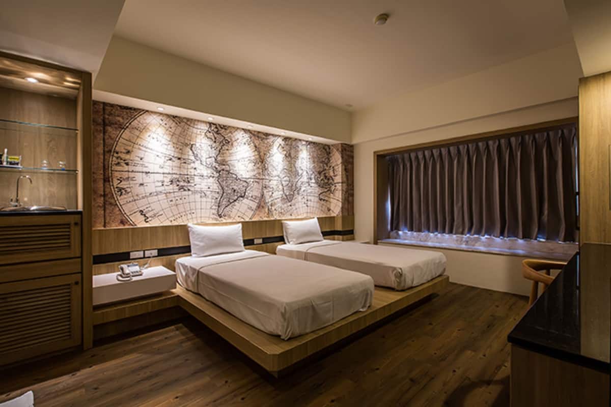 Quarto de hotel moderno com duas camas, um mural de um mapa-múndi, piso de madeira e uma janela com cortinas.
