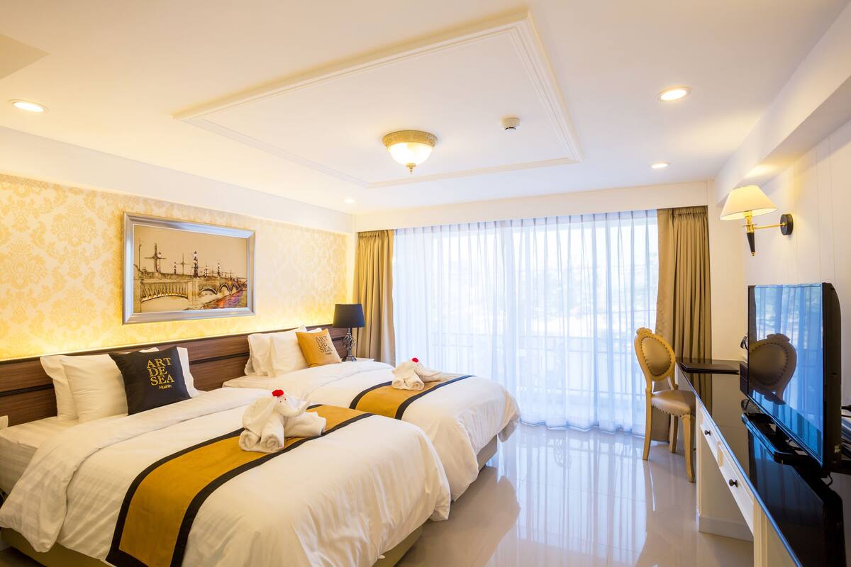 A hotel room with two beds, a desk with a television, and a painting on the wall.