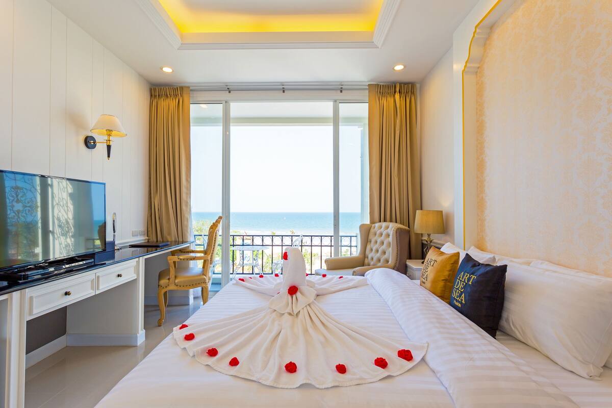 A hotel room with a bed, a desk, a television, a chair, and a view of the sea.