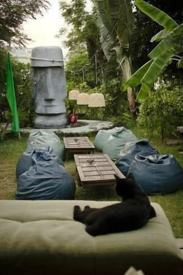 A garden with a large stone statue, bean bags, and a small table with a bowl.