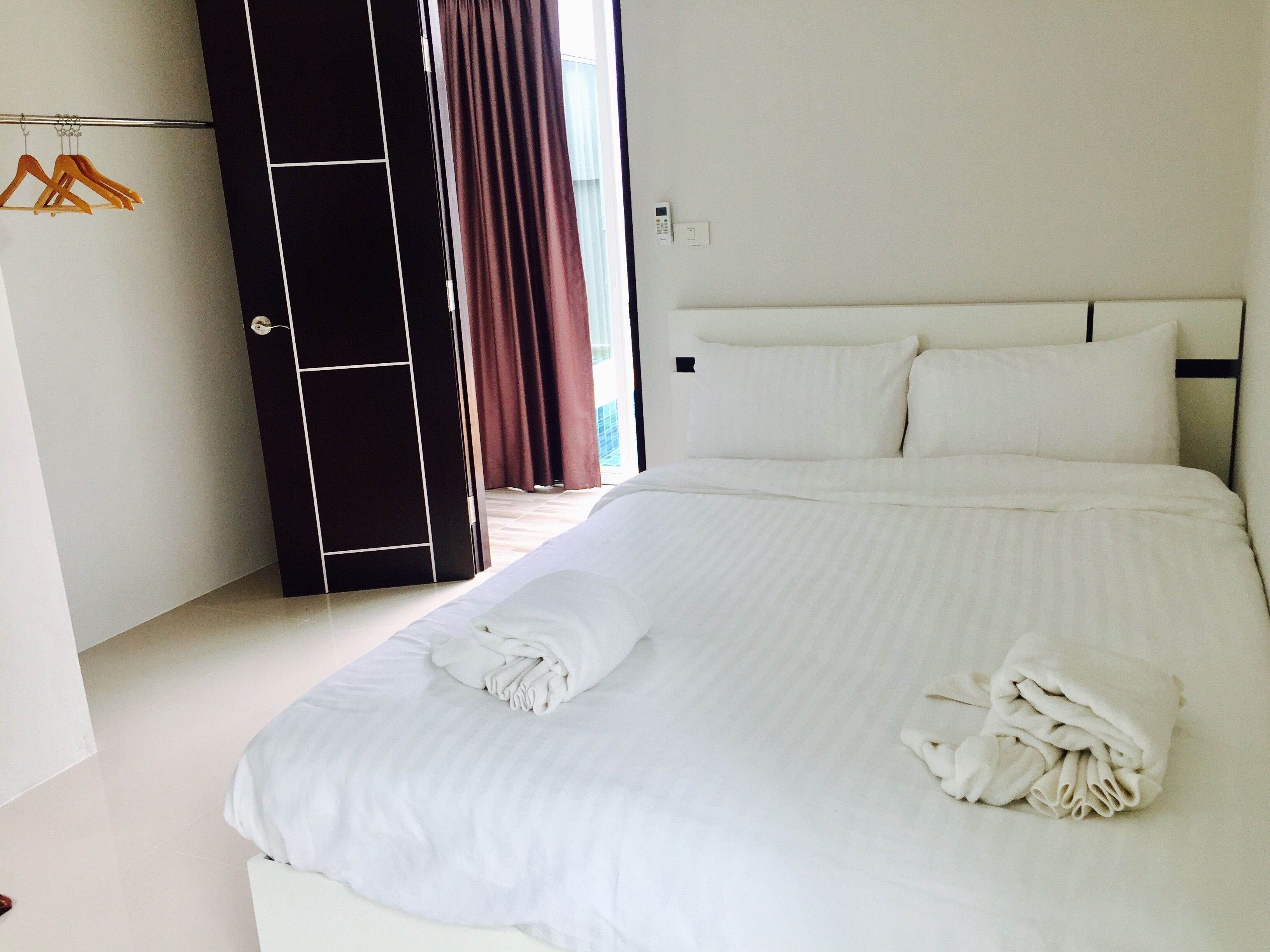 Een net opgemaakt bed met witte lakens en handdoeken, een zwarte garderobe met spiegel, en uitzicht op het omliggende landschap door een raam met gordijnen.