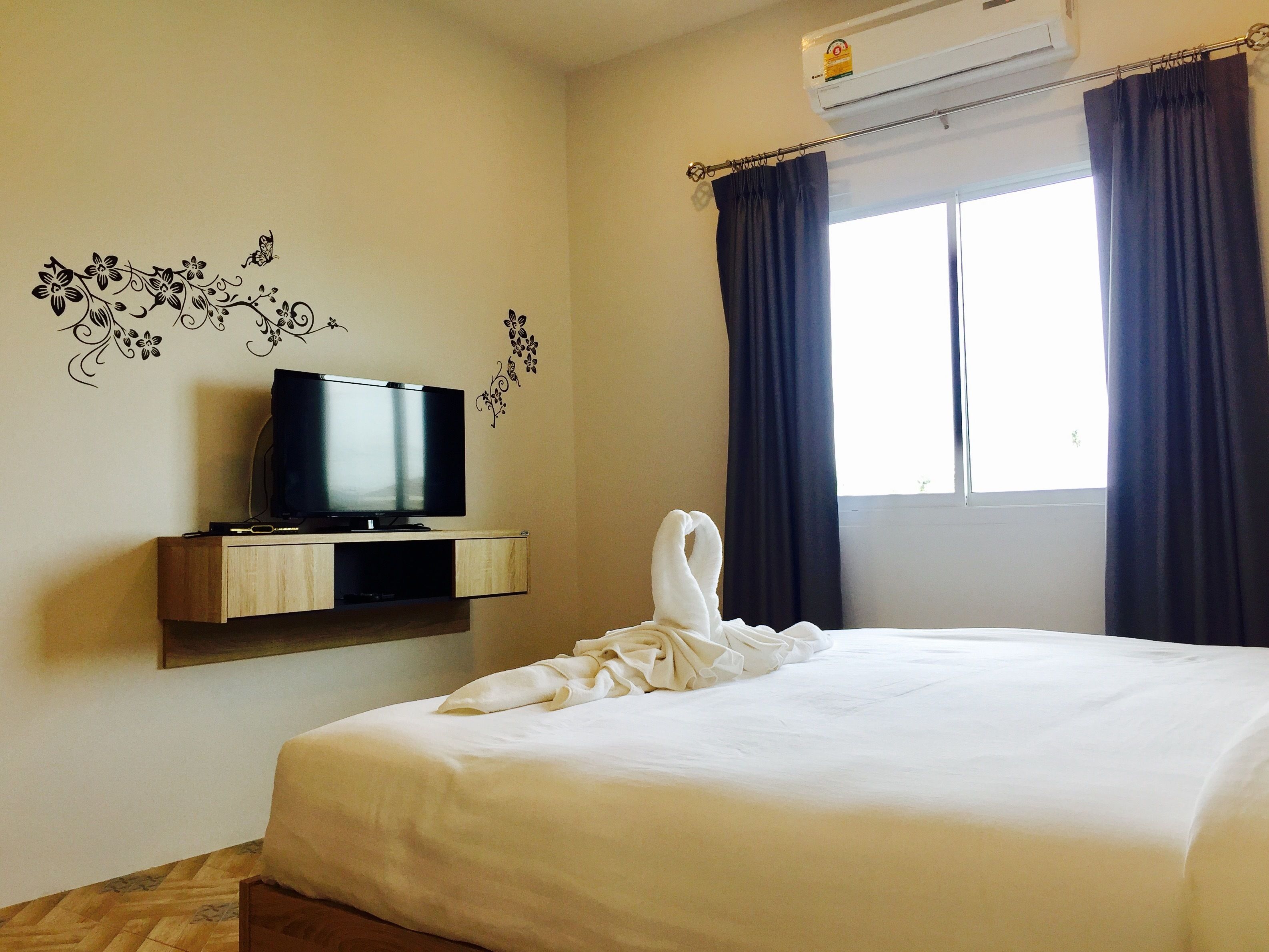 A hotel room with a bed, a flat-screen TV on a wooden shelf, a window with dark curtains, and wall decals.