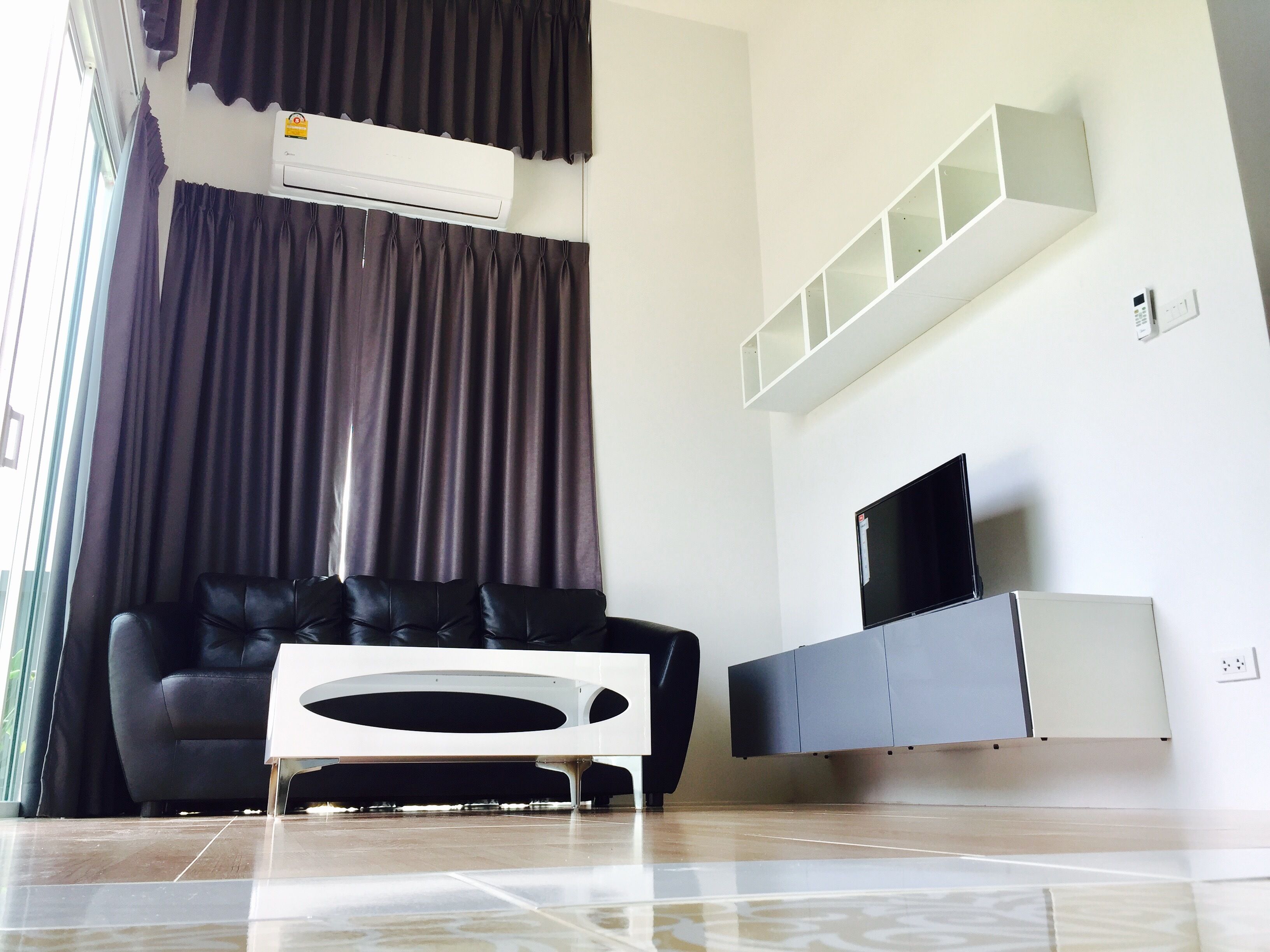 Una sala de estar moderna con un sofá de cuero negro, un mueble blanco para entretenimiento y un televisor de pantalla plana.