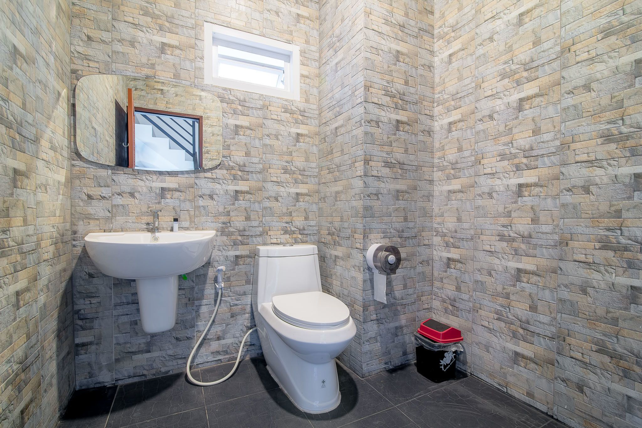 Un baño con pared de piedra, un lavamanos, un inodoro y un cubo de basura.
