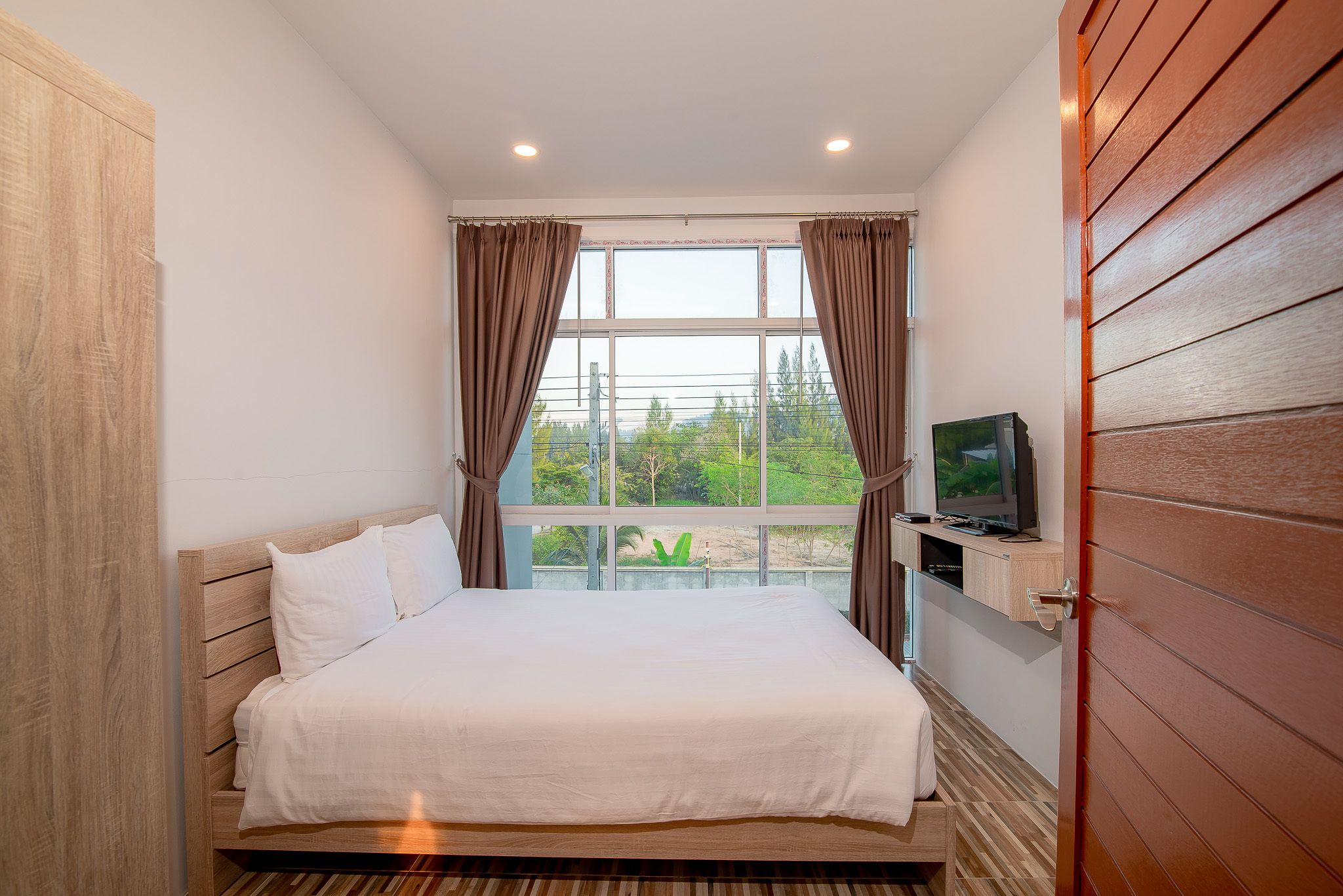 Une chambre à coucher avec un lit, un téléviseur posé sur une étagère et une fenêtre avec des rideaux.