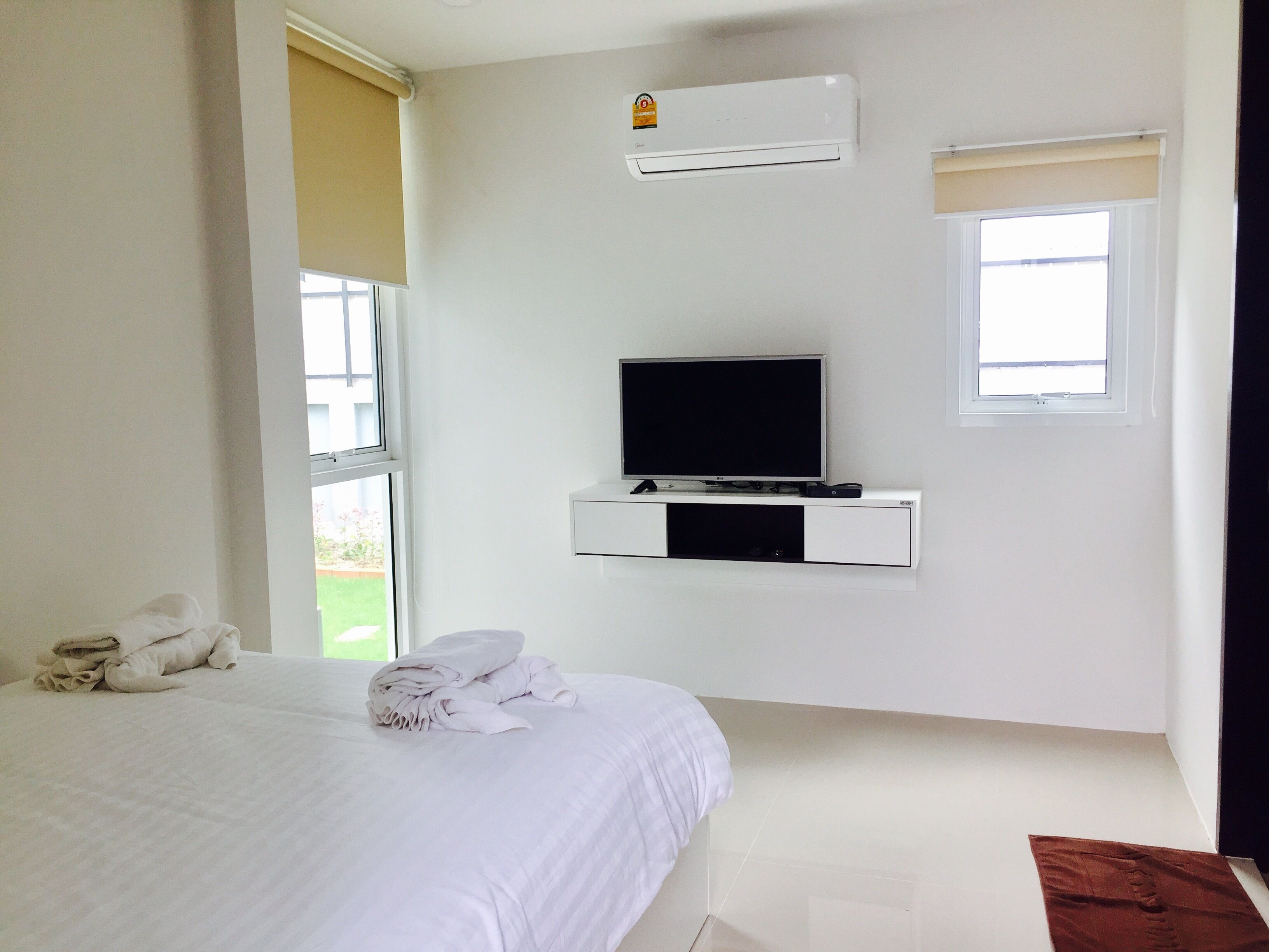 Ein Schlafzimmer mit einem Bett, einem an der Wand montierten Fernseher, einer Klimaanlage und einem Fenster.