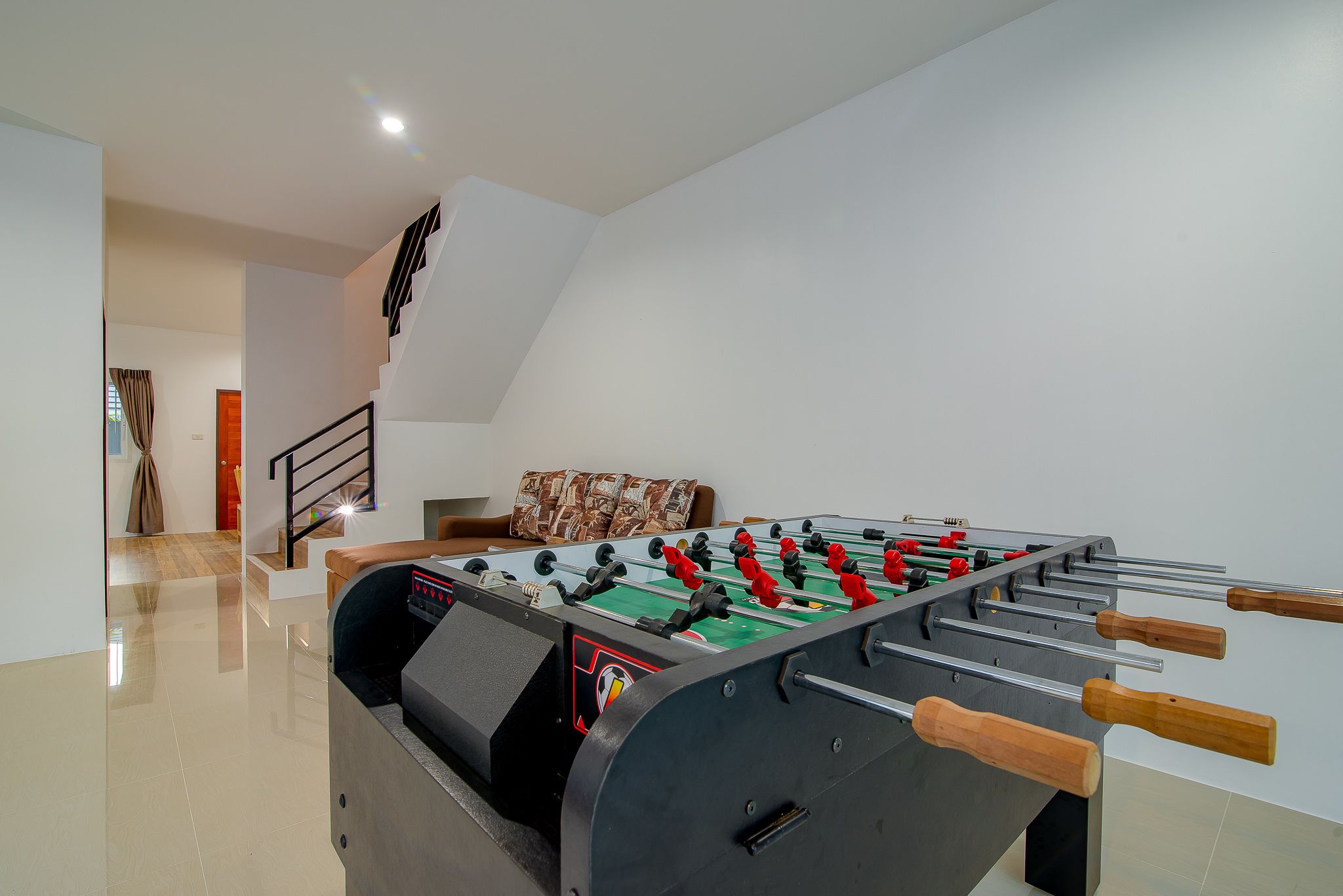 A modern indoor space with a foosball table, a staircase, and a couch.